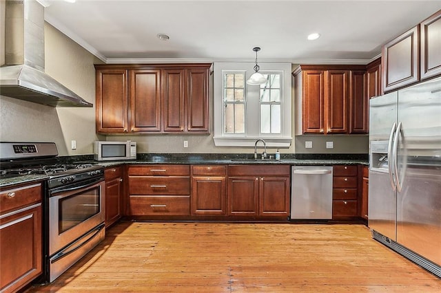 kitchen with wall chimney range hood, decorative light fixtures, appliances with stainless steel finishes, light wood-style flooring, and a sink