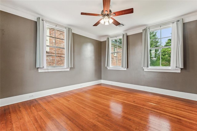 empty room with ceiling fan, baseboards, wood finished floors, visible vents, and crown molding