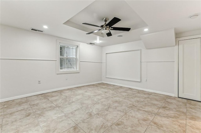 spare room with a raised ceiling, ceiling fan, baseboards, and visible vents