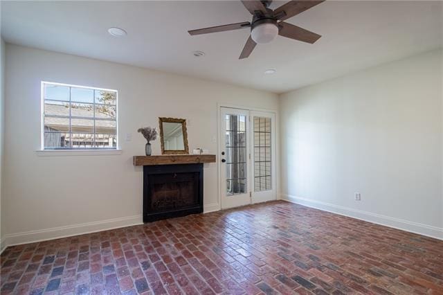 spare room with brick floor, a fireplace, a ceiling fan, and baseboards