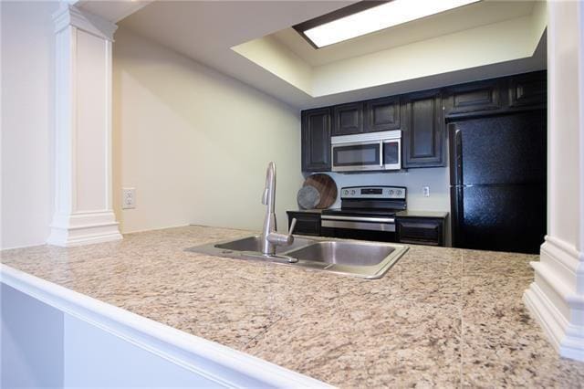 kitchen featuring decorative columns, stainless steel appliances, a sink, dark cabinets, and a peninsula