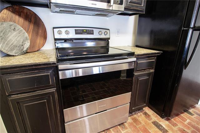 kitchen with appliances with stainless steel finishes, brick floor, dark brown cabinetry, and light stone countertops