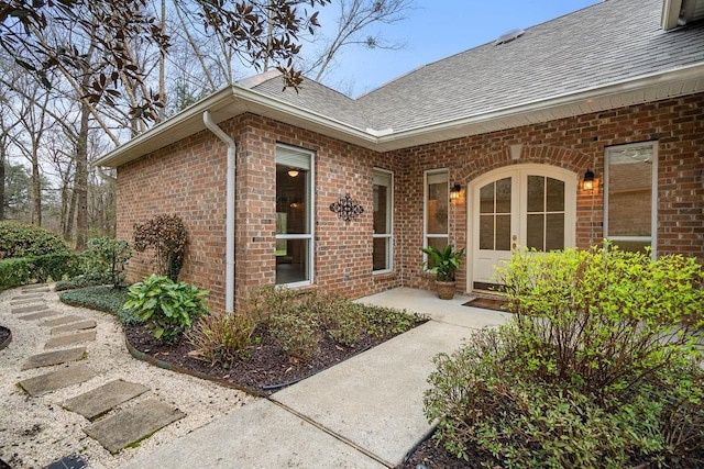 property entrance featuring brick siding, roof with shingles, and a patio area