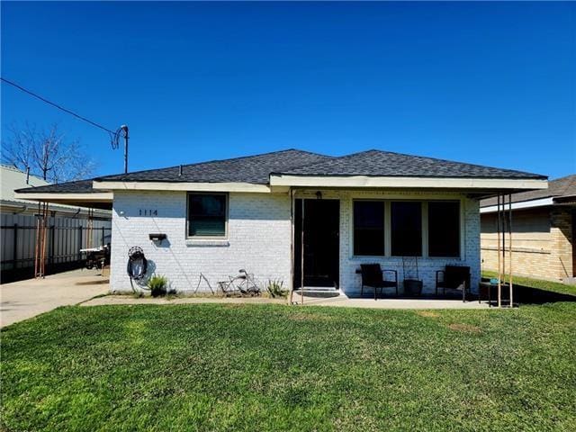 rear view of property with a yard, an attached carport, brick siding, and fence