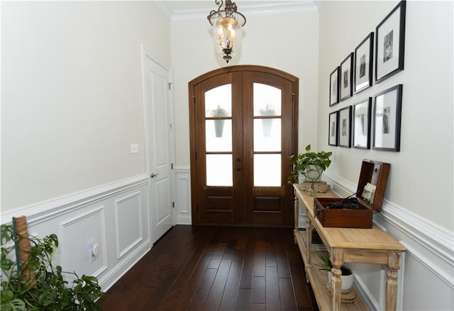 foyer with arched walkways, a wainscoted wall, ornamental molding, dark wood-style flooring, and french doors