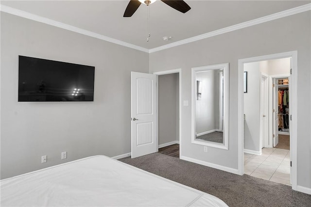 bedroom with carpet floors, a walk in closet, crown molding, a ceiling fan, and baseboards