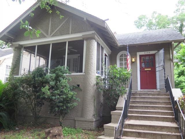 exterior space with a shingled roof, a sunroom, stairway, and stucco siding