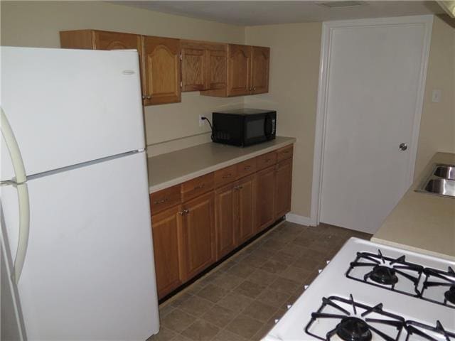 kitchen with brown cabinets, white appliances, light countertops, and a sink