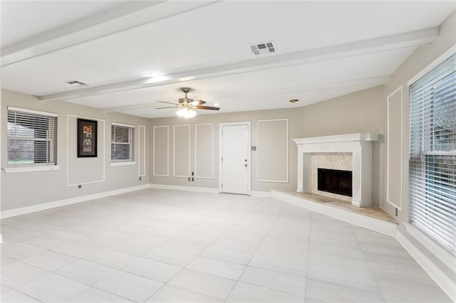 unfurnished living room with a high end fireplace, beam ceiling, visible vents, and baseboards