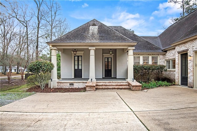 view of front of property featuring stucco siding, roof with shingles, crawl space, covered porch, and brick siding