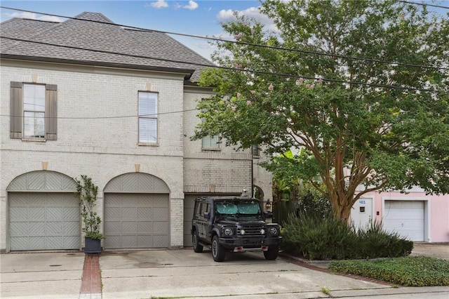 view of front of home with a garage, concrete driveway, brick siding, and roof with shingles