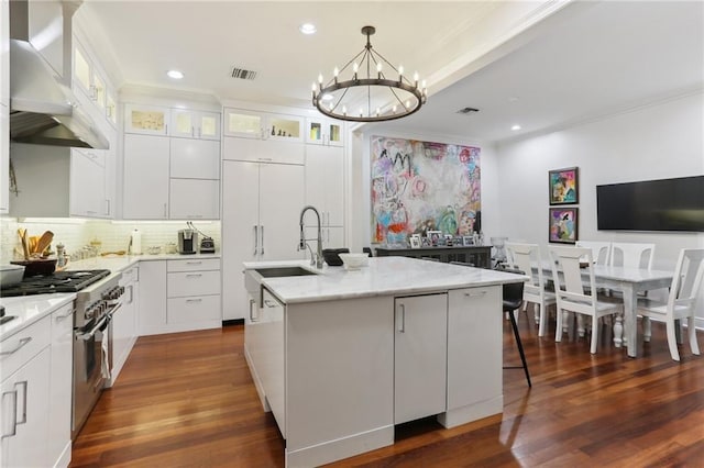 kitchen featuring glass insert cabinets, white cabinets, a center island with sink, and ventilation hood