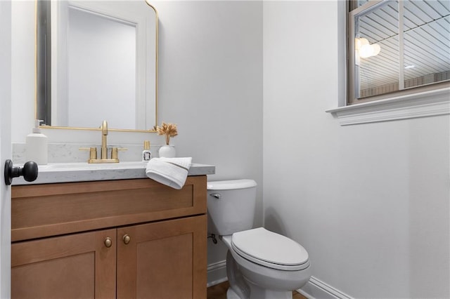 half bathroom with toilet, baseboards, and vanity