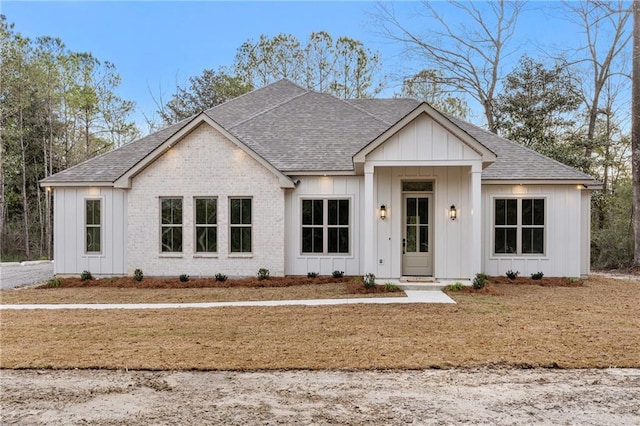 modern farmhouse style home with a shingled roof, board and batten siding, and brick siding