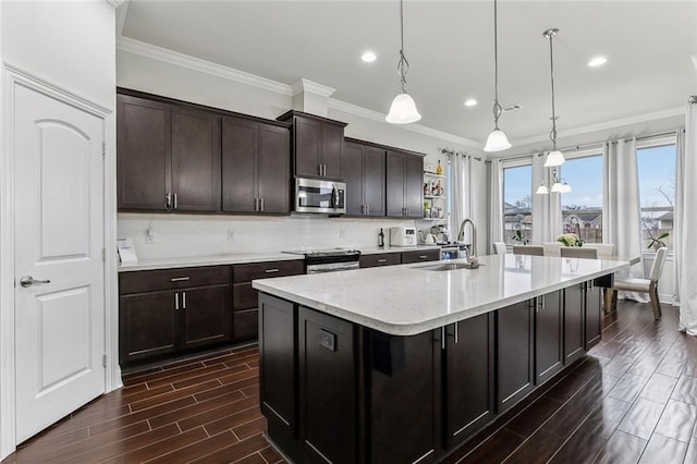 kitchen featuring pendant lighting, a center island with sink, light countertops, appliances with stainless steel finishes, and a sink