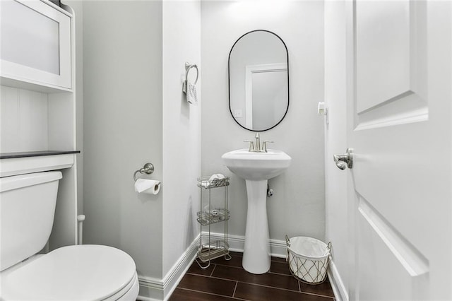 half bathroom featuring toilet, wood tiled floor, baseboards, and a sink