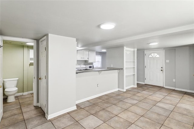 5116 Franklin Ave, New Orleans, LA 70122 - kitchen with light tile patterned floors, under cabinet range hood, white cabinets, white microwave, and a breakfast bar area