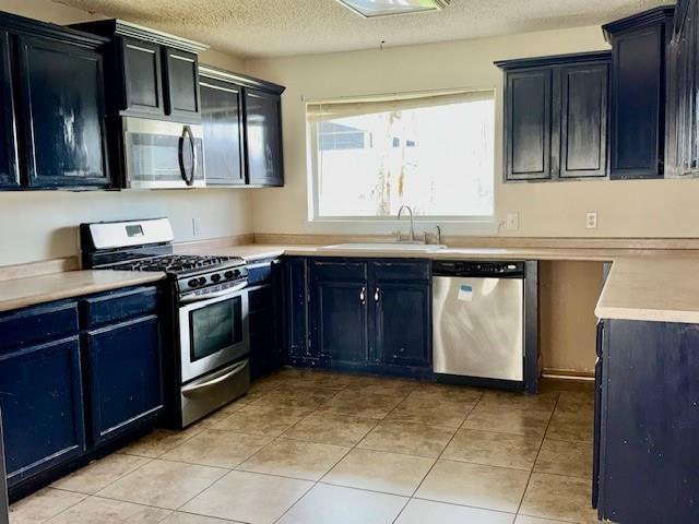 kitchen featuring stainless steel appliances, light countertops, a sink, and dark cabinetry