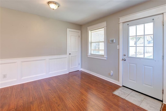 foyer with a wainscoted wall, a decorative wall, and light wood-style flooring