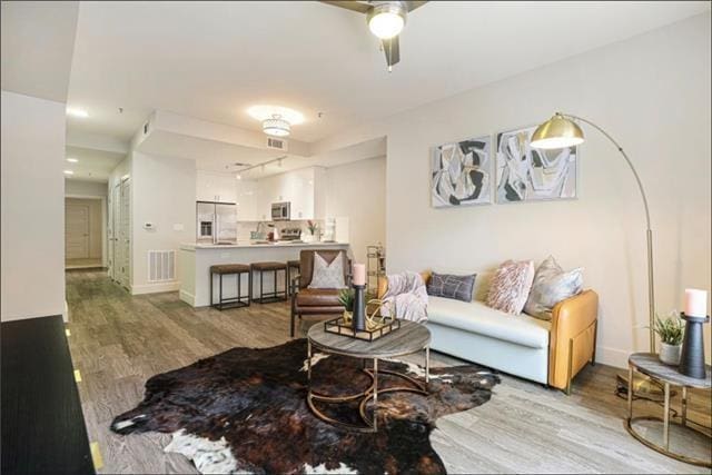 living area with a ceiling fan, baseboards, visible vents, and wood finished floors