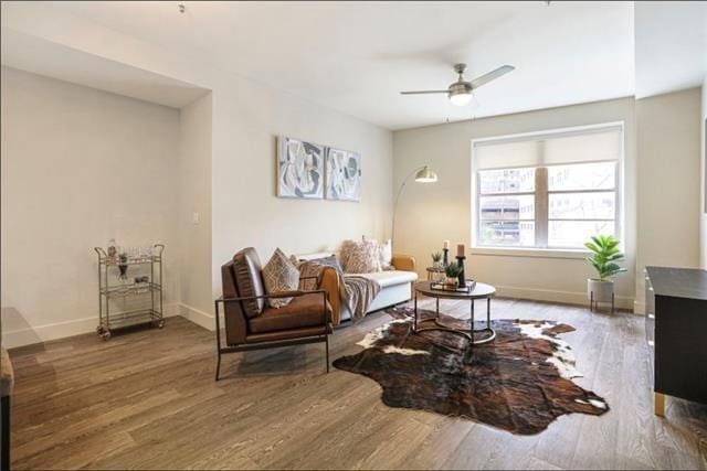 living area featuring ceiling fan, baseboards, and wood finished floors