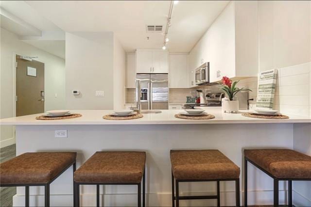 kitchen featuring a kitchen bar, white cabinetry, stainless steel appliances, and light countertops