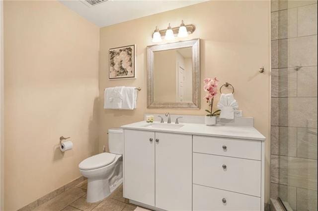 bathroom with baseboards, toilet, tile patterned flooring, a tile shower, and vanity