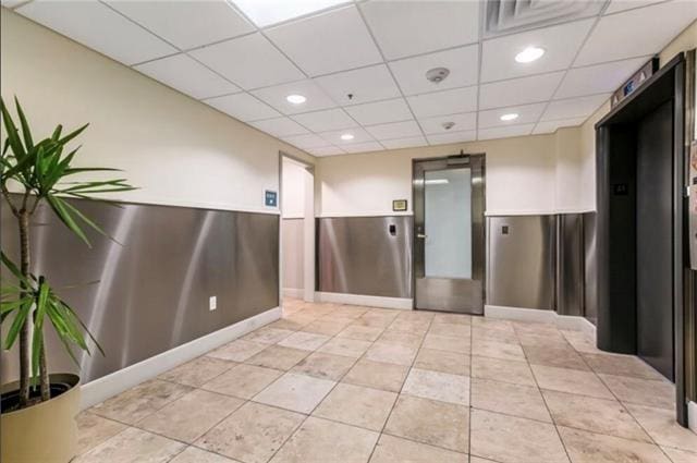 empty room with a paneled ceiling, elevator, light tile patterned flooring, and recessed lighting
