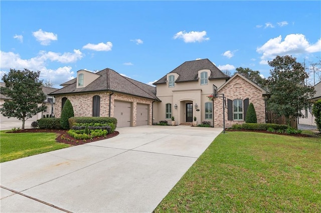 french provincial home with driveway, stucco siding, an attached garage, a front yard, and brick siding