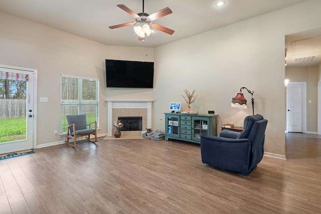 living room featuring a ceiling fan, a fireplace, baseboards, and wood finished floors