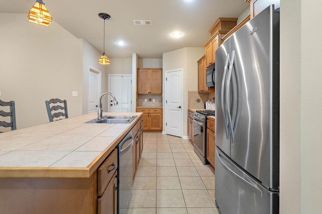 kitchen featuring light tile patterned floors, tile counters, an island with sink, stainless steel appliances, and a sink