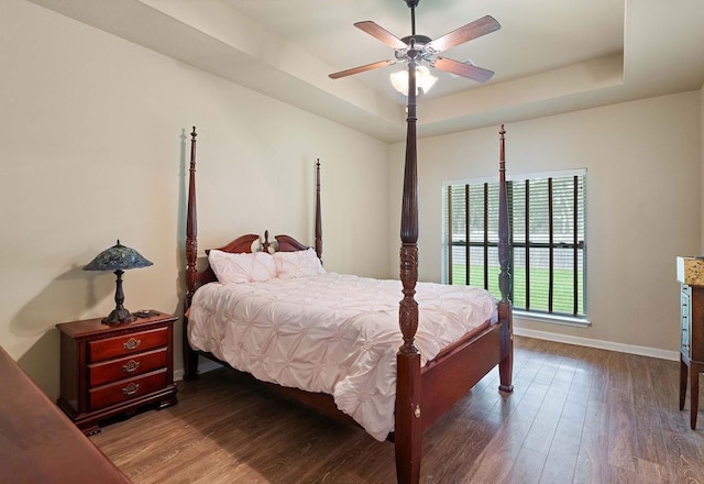 bedroom featuring a ceiling fan, baseboards, a tray ceiling, and wood finished floors