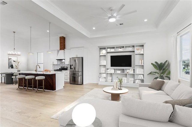 living area featuring light wood-style floors, ceiling fan, a tray ceiling, and recessed lighting