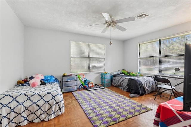 bedroom with ceiling fan, multiple windows, a textured ceiling, and visible vents