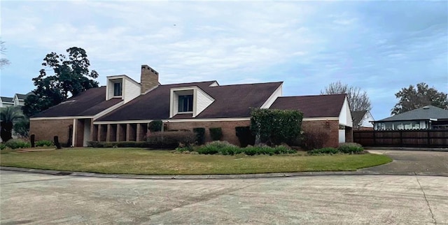 view of front of home featuring brick siding, a chimney, a front yard, fence, and driveway