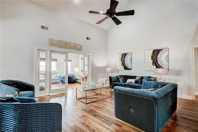 living room featuring high vaulted ceiling, visible vents, baseboards, and wood finished floors