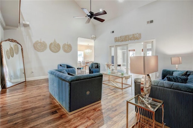 living area with a towering ceiling, visible vents, wood finished floors, and ceiling fan with notable chandelier