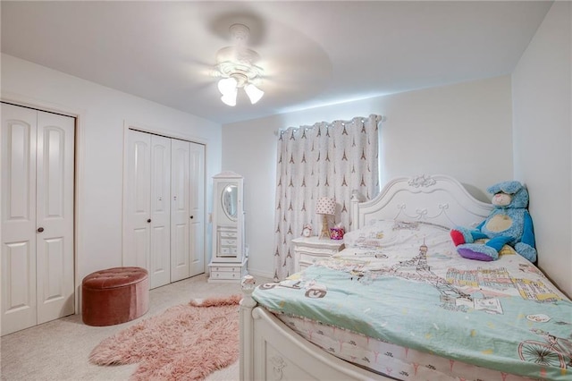 bedroom featuring light colored carpet, ceiling fan, and two closets