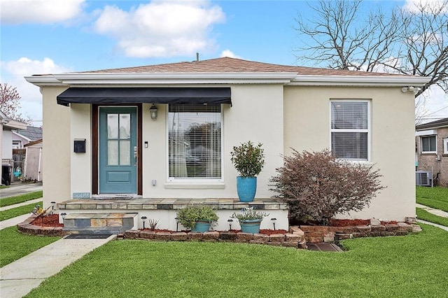 bungalow featuring a shingled roof, central AC, a front lawn, and stucco siding