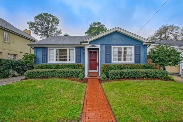 bungalow featuring a front lawn and stucco siding