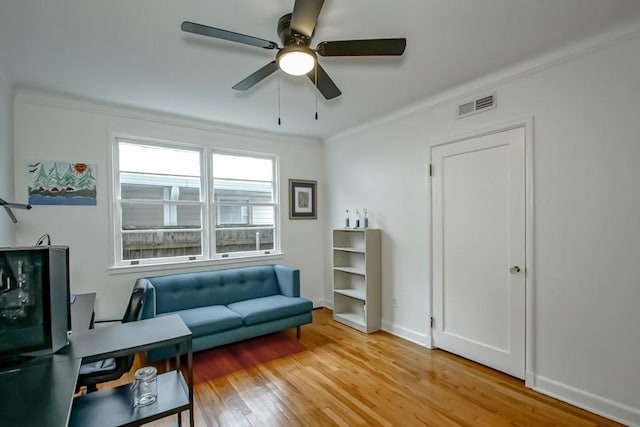 living area with wood finished floors, a ceiling fan, visible vents, baseboards, and crown molding