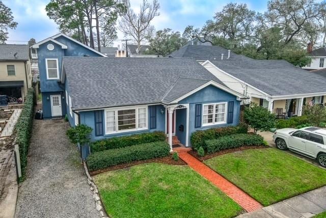 view of front of property featuring a shingled roof, a front yard, and stucco siding