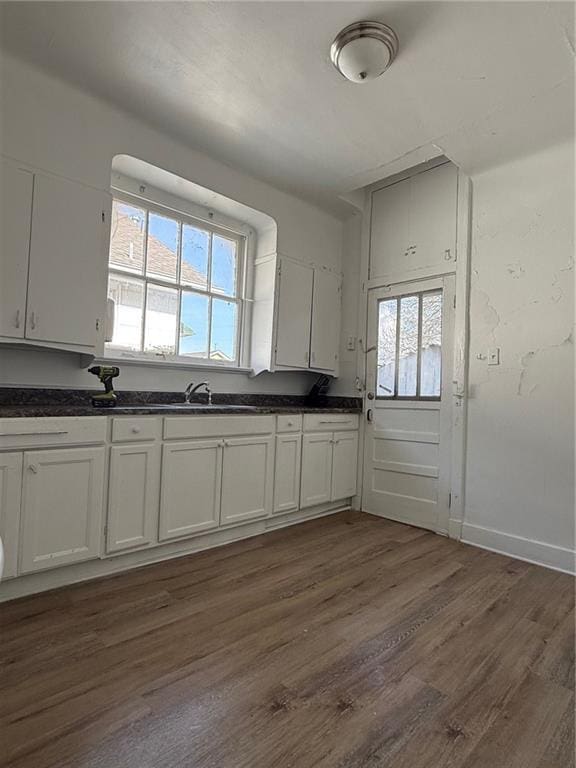 kitchen with dark wood-type flooring, dark countertops, white cabinetry, and baseboards