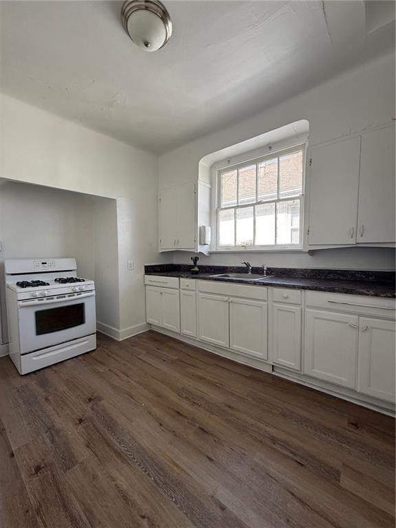 kitchen with dark wood finished floors, gas range gas stove, dark countertops, white cabinets, and a sink