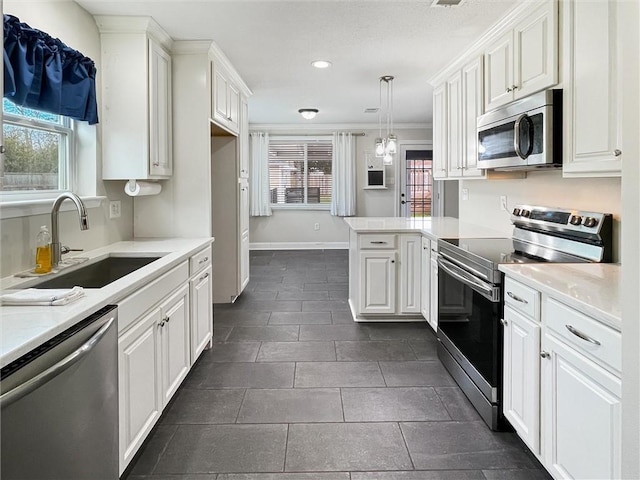 kitchen featuring pendant lighting, light countertops, appliances with stainless steel finishes, white cabinetry, and a sink