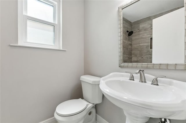 bathroom with a tile shower, a sink, toilet, and baseboards