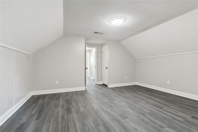 bonus room with visible vents, dark wood-type flooring, vaulted ceiling, a textured ceiling, and baseboards