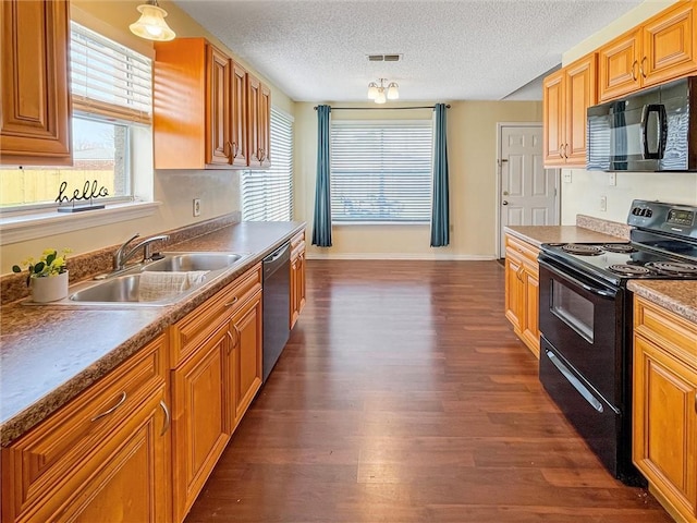 kitchen with brown cabinetry, dark wood finished floors, a sink, and black appliances