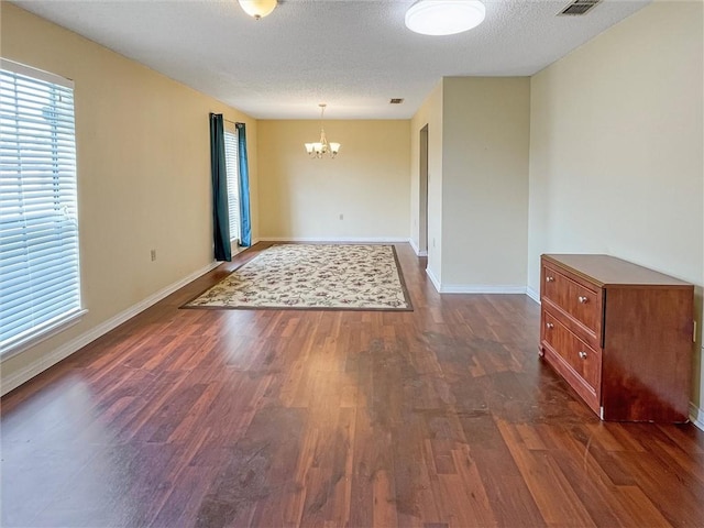 empty room featuring a textured ceiling, visible vents, baseboards, dark wood-style floors, and an inviting chandelier