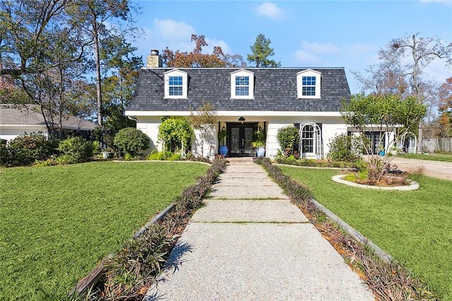 front of property with a shingled roof, a front yard, a chimney, and mansard roof